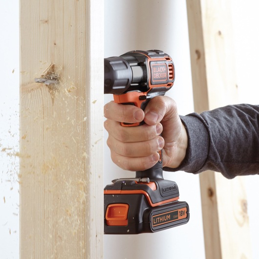 BLACK+DECKER ASD18KB cordless drill in use, drilling through wood, side angle view.