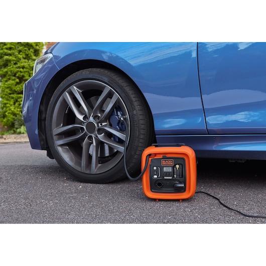 BLACKDECKER ASI400 portable tire inflator next to blue car, hose connected to car tire on paved surface.