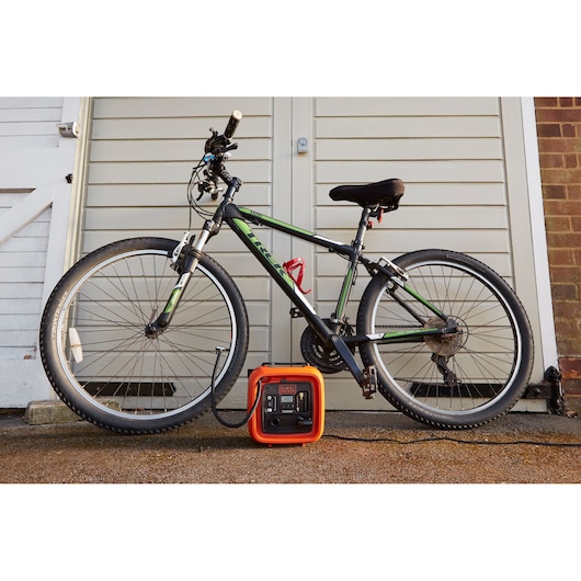 BLACKDECKER ASI400 portable air compressor shown inflating a bicycle tire outdoors.