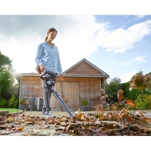BLACKDECKER BCASBL71B leaf blower in use clearing leaves outdoors near wooden shed.