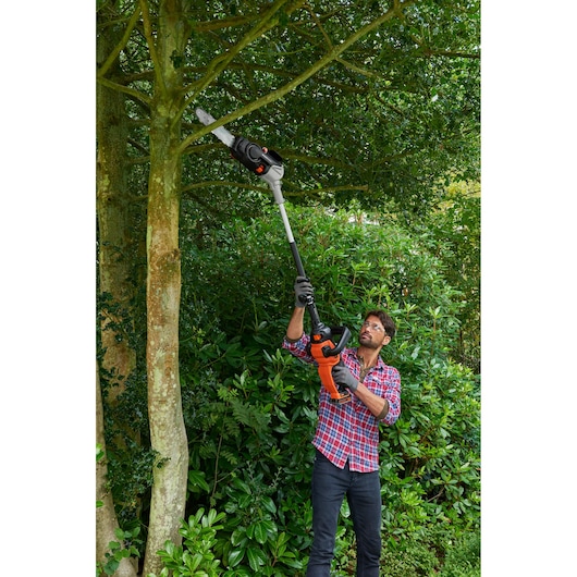 BLACKDECKER BCASCS61B pole saw used to trim high tree branches outdoors, shown in action close-up.