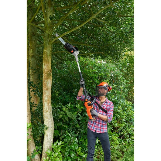 BLACKDECKER BCASCS61B pole saw trimming high tree branches in leafy garden.