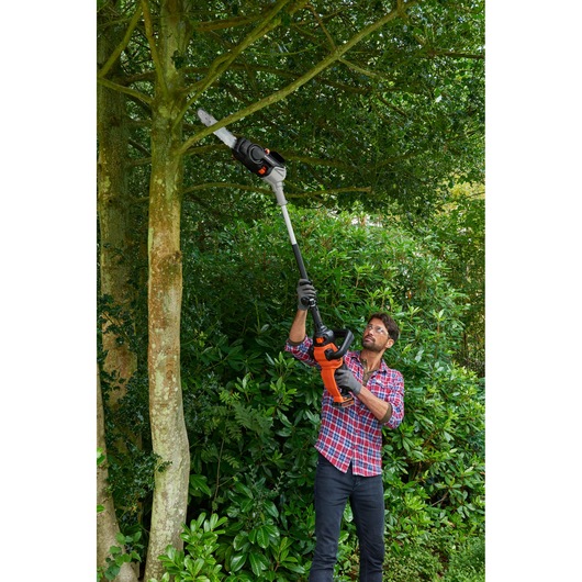 BLACK+DECKER BCASK861D pole saw used for trimming high tree branches in a garden.