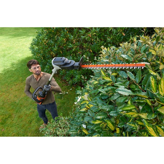 Photo of BLACKDECKER BCASK861D hedge trimmer in use trimming green bushes outdoors.