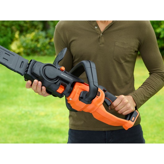 BLACK+DECKER BCASK861D chainsaw with orange and black body held outdoors by person in green shirt.