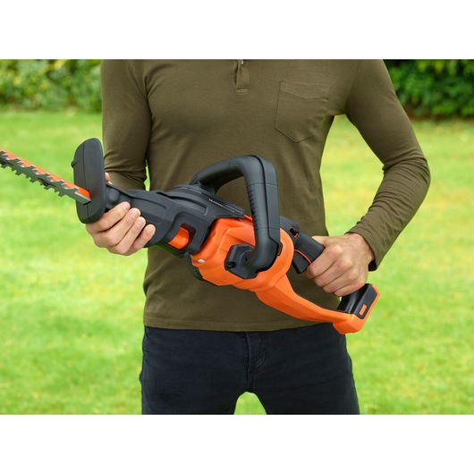 BLACKDECKER BCASK861D hedge trimmer in use, shown in hands outdoors, orange and black body, close-up view.