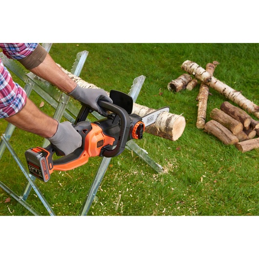 BLACK+DECKER BCASK861D chainsaw cutting log, user wearing gloves, outdoor on grass.