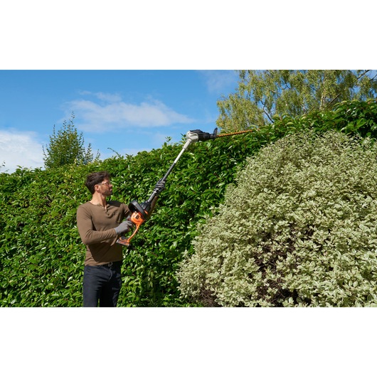 BLACKDECKER BCASK861D hedge trimmer in use outdoors trimming tall green hedge.