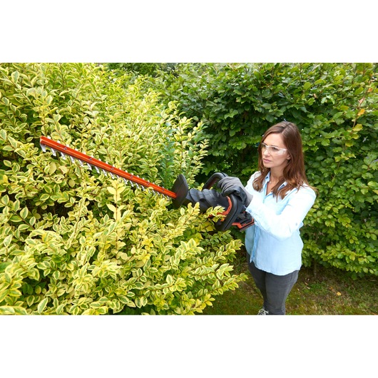 BLACKDECKER BCASK861D hedge trimmer in use trimming green bushes outdoors.