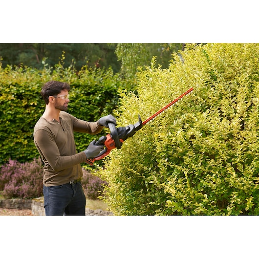 BLACKDECKER hedge trimmer BCASK891D in use trimming yellow-green bush outdoors.