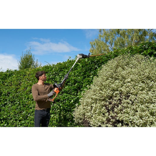 BLACKDECKER BCASK891D hedge trimmer in use outdoors, person trimming tall green hedge.