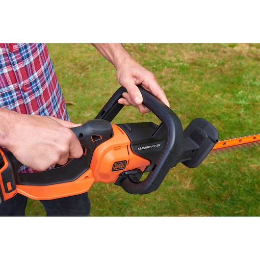 BLACK+DECKER BCASK8967D2 hedge trimmer in use, orange and black design, shown outdoors cutting grass.