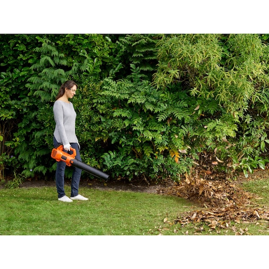 Person using BLACKDECKER BCBL200L cordless leaf blower on garden leaves, orange and black in color.