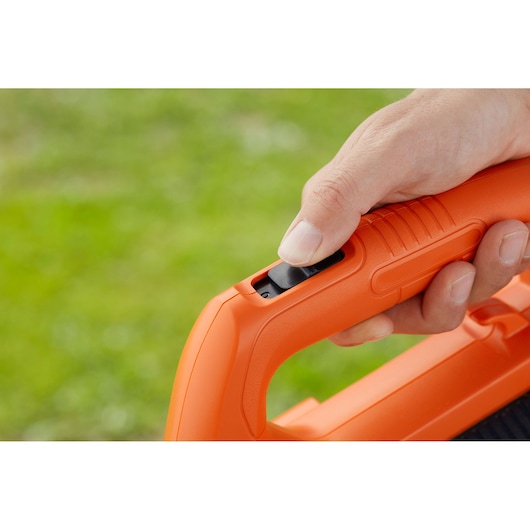 Close-up photo of a hand pressing the trigger on an orange BLACK+DECKER BCBL200L blower handle.