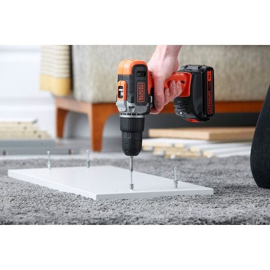 Photo of BLACKDECKER cordless drill BCD003C1C assembling furniture, driving screw into white board on carpet.