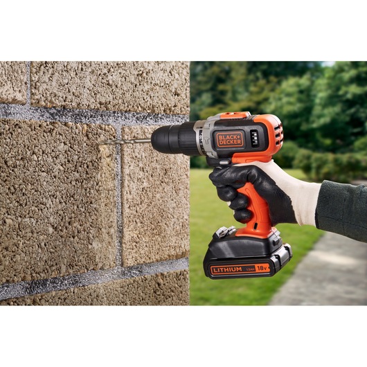 BLACKDECKER BCD003C1C cordless drill in use drilling into stone wall, orange and black design, outdoor setting.