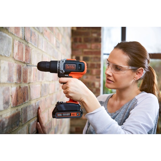 Photo of BLACK+DECKER BCD003C1C cordless drill in use, drilling into a brick wall.