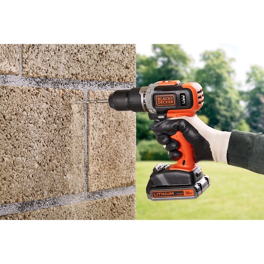 BLACKDECKER cordless drill BCD003MEM2K, orange and black, drilling into a stone wall outdoors.