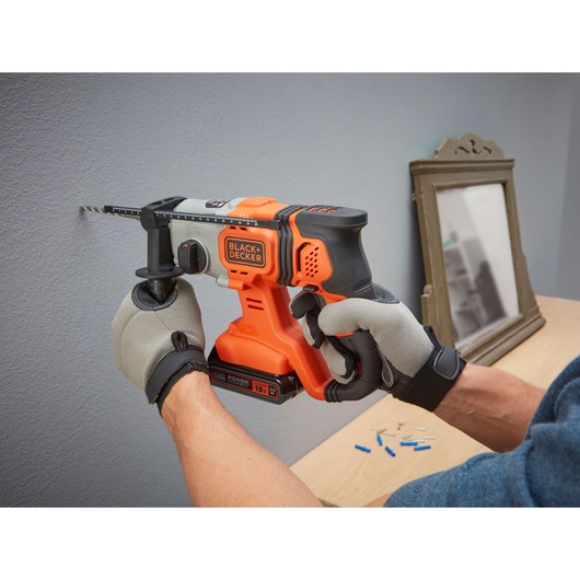 Photo of BLACK+DECKER BCD900E2K cordless hammer drill in use on a wall, orange and black design, gloved hands.