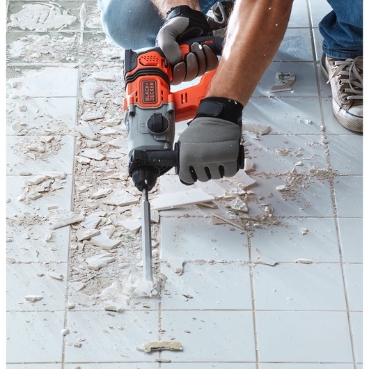 BLACK+DECKER BCD900M1K rotary hammer in use for tile removal on a white tiled floor, close-up angle.