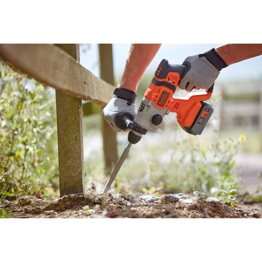 Photo of BLACKDECKER BCD900M1K rotary hammer drill used outdoors on concrete, gloved hands holding tool.