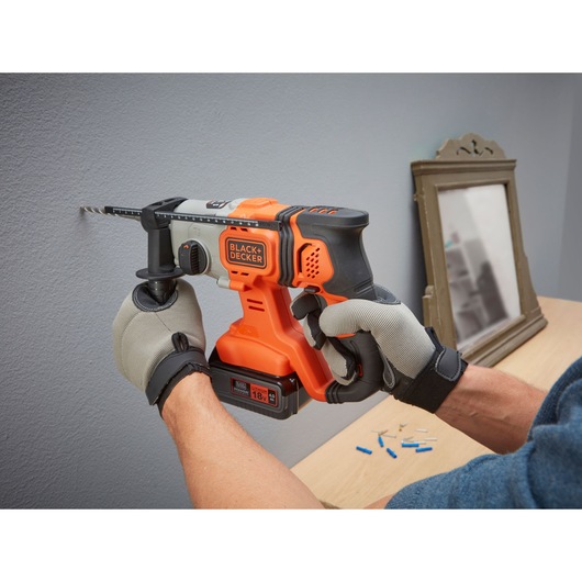 BLACKDECKER BCD900M1K cordless hammer drill being used on a wall, person wearing gloves.