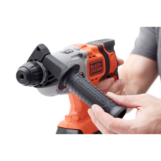 Photo of BLACK+DECKER BCD900M1K cordless hammer drill in orange and black, shown in use from a side angle.