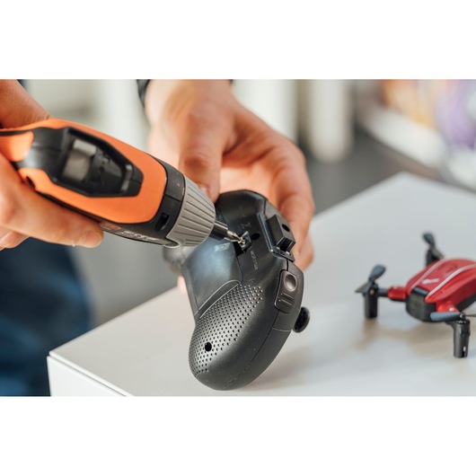 BLACKDECKER BCF611CK cordless screwdriver used on a black remote control beside a red drone.