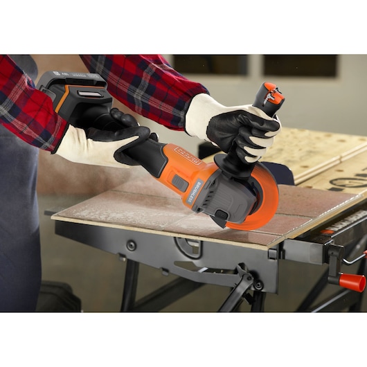 BLACKDECKER BCG6L8D2S cordless angle grinder in use cutting tile, worker wearing gloves and plaid shirt.