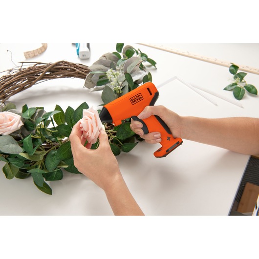 Photo of BLACKDECKER BCGL115OB cordless glue gun used to attach flowers to a wreath on a white table.