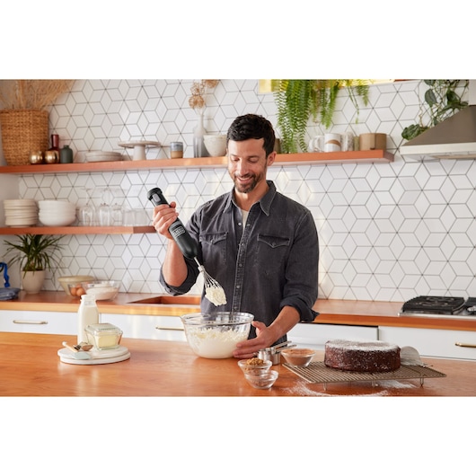 BLACKDECKER BCKM1012KB hand mixer used in kitchen with cake and ingredients on wooden countertop.