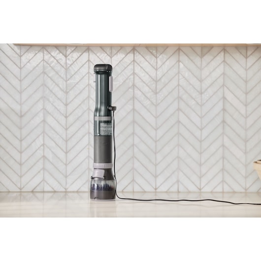 BLACKDECKER BCKM1012KB cordless vacuum standing upright on a kitchen counter, side view, charger cable attached.