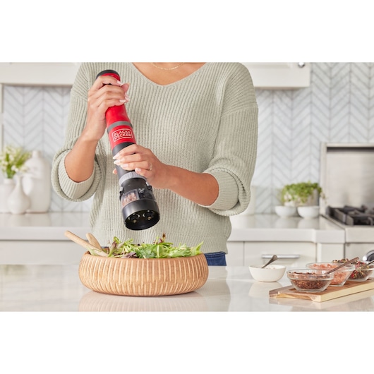 Photo of a person using a BLACKDECKER electric pepper grinder BCKM1012KR to season a salad in a wood bowl.