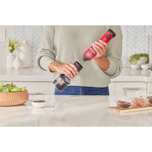 Photo of BLACK+DECKER BCKM1012KR red cordless electric grinder held over a kitchen counter near salad and spices.