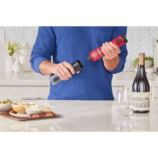 BLACKDECKER BCKM1012KR electric wine opener in use on a kitchen counter near wine glasses and a bottle.