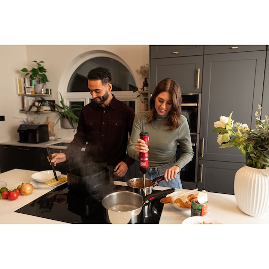 BLACKDECKER BCKM1012KR red hand blender used by a woman in a modern kitchen, man cooking beside her.