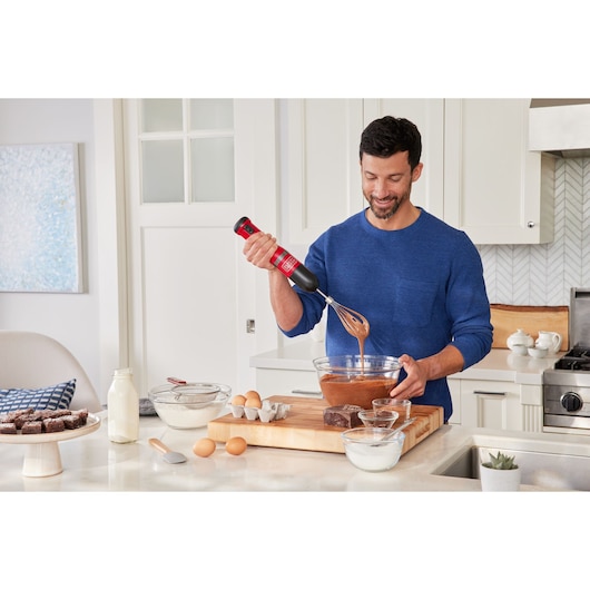 BLACKDECKER BCKM1012KR hand mixer used to mix batter in a glass bowl on a kitchen counter.