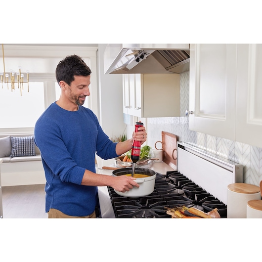 BLACKDECKER BCKM1016KSR red hand blender in use blending soup in a white pot on kitchen stove.