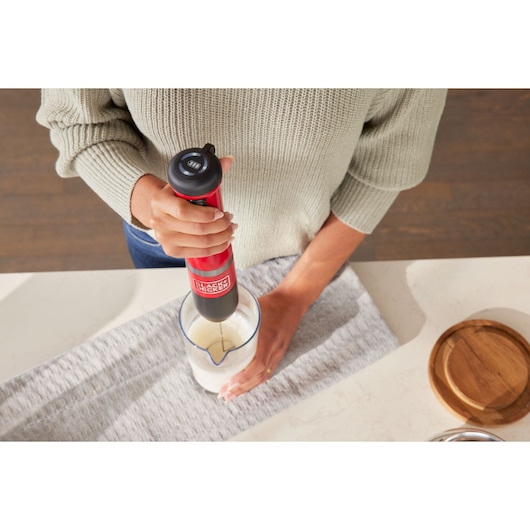 BLACKDECKER BCKM1016KSR hand blender in red being used to mix ingredients in a glass measuring cup on a kitchen counter.