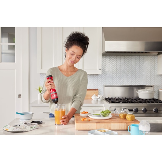 BLACKDECKER BCKM1016KSR handheld mixer blending orange liquid in a glass in a modern kitchen.