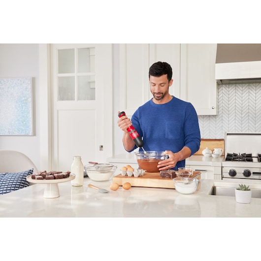 Photography of BLACKDECKER BCKM1016KSR hand mixer in use mixing ingredients in a glass bowl in a modern kitchen.