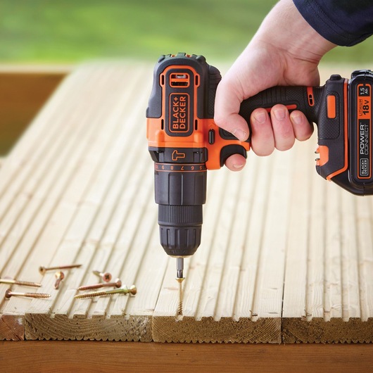 BLACK+DECKER BCKSB04 cordless drill in use driving a screw into wood, visible hand holding tool, outdoor setting.