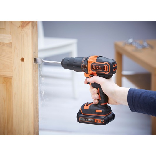 BLACKDECKER BCKSB04 cordless drill in use drilling a wooden door, orange and black, side angle.