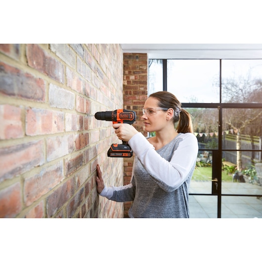 Person using BLACKDECKER BCKSB05 cordless drill on brick wall indoors, photo shows side profile with drill in action.