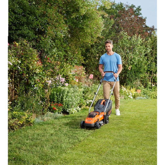Photo of BLACKDECKER BCMW3336L1 lawn mower in use on a garden lawn, orange and black, outdoor setting.