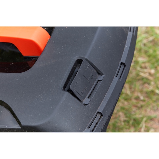 Close-up photo of BLACKDECKER BCMW3336L2 lawn mower stop/start button on black casing, outdoor setting.