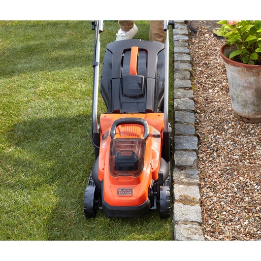 BLACKDECKER BCMW3336N lawn mower front view on grass next to stone border and flower pot.