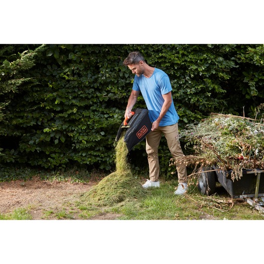 BLACKDECKER lawn mower BCMW3336N grass catcher bin being emptied outdoors by a person.