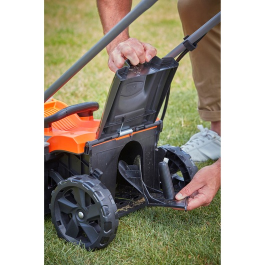 BLACKDECKER BCMW3336N lawn mower with open rear chute on grass, showing maintenance access.