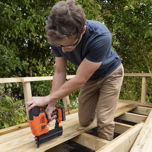 BLACKDECKER BCNG01N cordless nail gun used to secure wooden planks on outdoor decking.